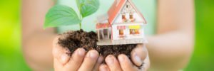 Child in a green top holding a small house and plant in her hands