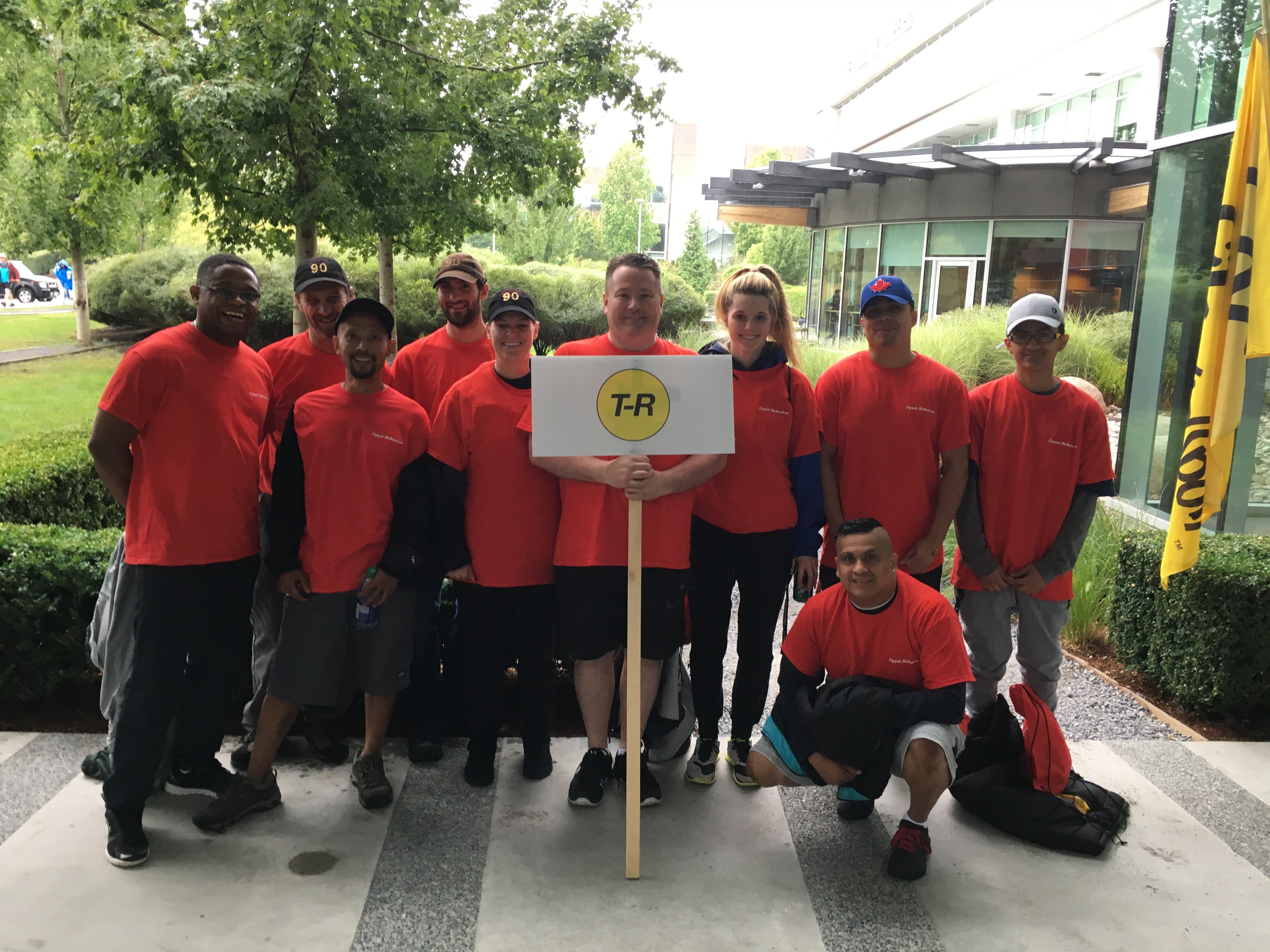 All T-R staff wearing red t-shirts in front of a building holding up a white T-R sign for the Corporate Kids Challenge 2017