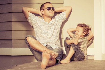 Father and son taking in the sun outside their new home, while both wearing collar shirts and jean shorts