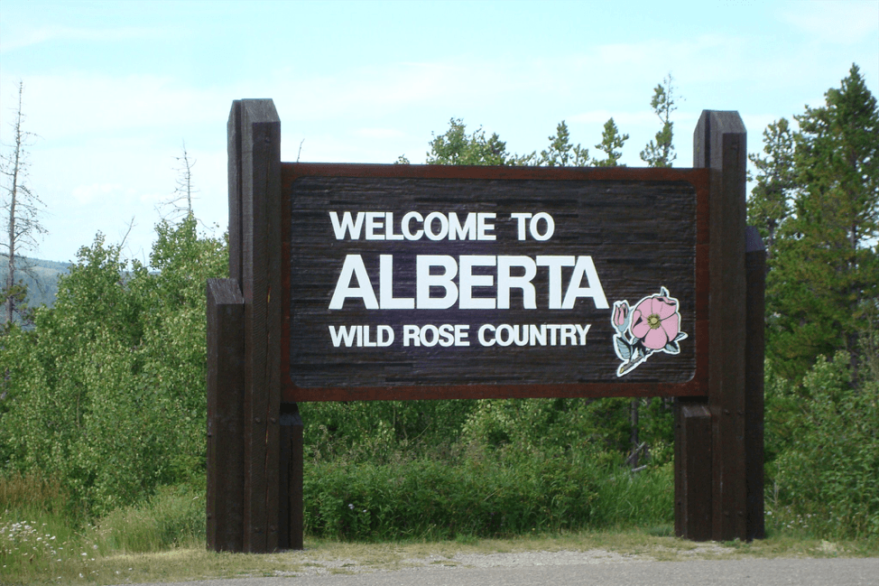 Wooden Alberta tourism logo sign that displays Welcome to Alberta Wild Rose Country