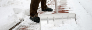 Man, wearing a brown pair of pants and black shoes is shoveling snow off his pathway to his front door