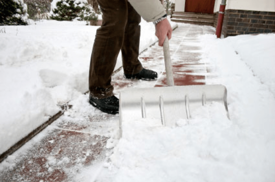 Man, wearing a brown pair of pants and black shoes is shoveling snow off his pathway to his front door