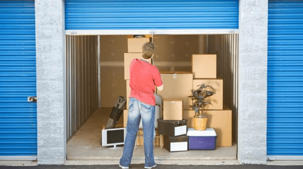 Man, wearing a red top and blue jeans is in front of a storage unit, storing office files, boxes and computer equipment