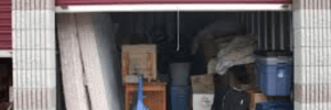 Maroon colored storage unit filled with personal belongings, two mattresses, blue vacuum, suitcases