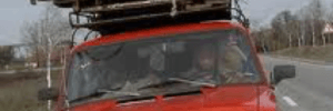 Man, in an old red car, trying to move his personal belongings that is tied on the roof of his car