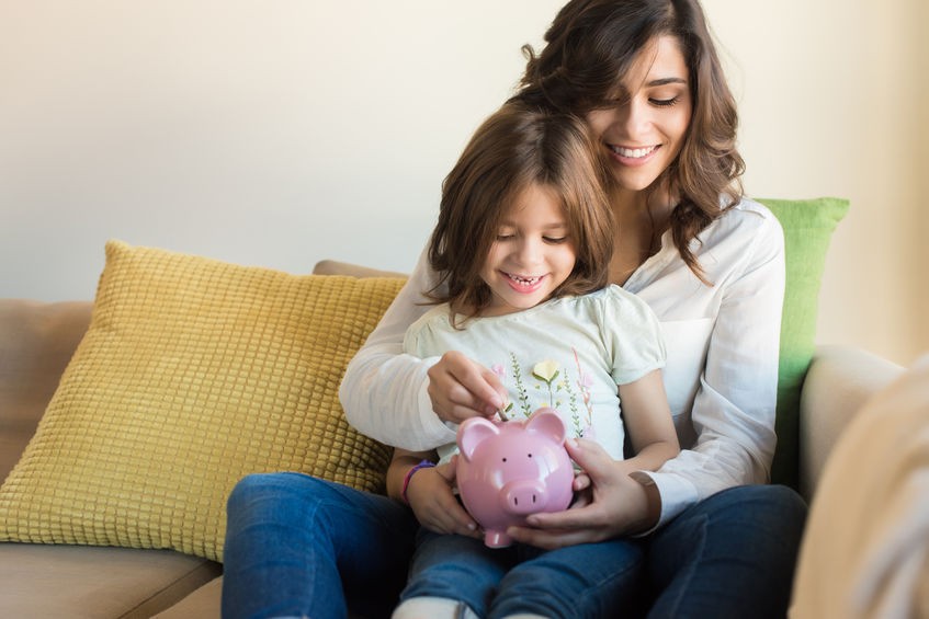 Lady with her daughter sitting on a couch holding a pink piggy bank